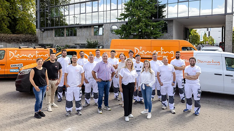 Team eines Malerbetriebs der HPM DIE HANDWERKSGRUPPE vor Firmenstandort mit Servicefahrzeugen