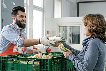Helfer einer deutschen Tafel reicht einer Frau ein Lebensmittelpaket