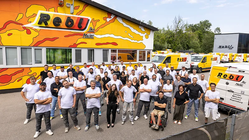 Großes Team eines Handwerksbetriebs der HPM DIE HANDWERKSGRUPPE vor Firmengebäude und Servicefahrzeugen