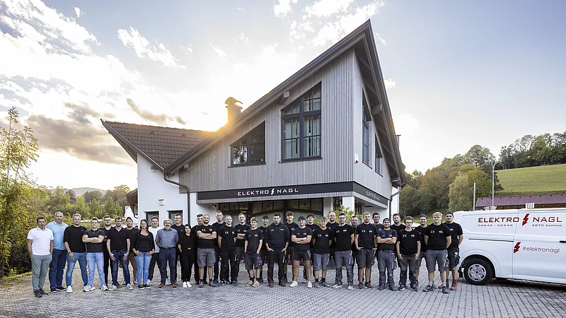 Team eines Elektro-Handwerksbetriebs der HPM DIE HANDWERKSGRUPPE vor Firmengebäude und Servicefahrzeug